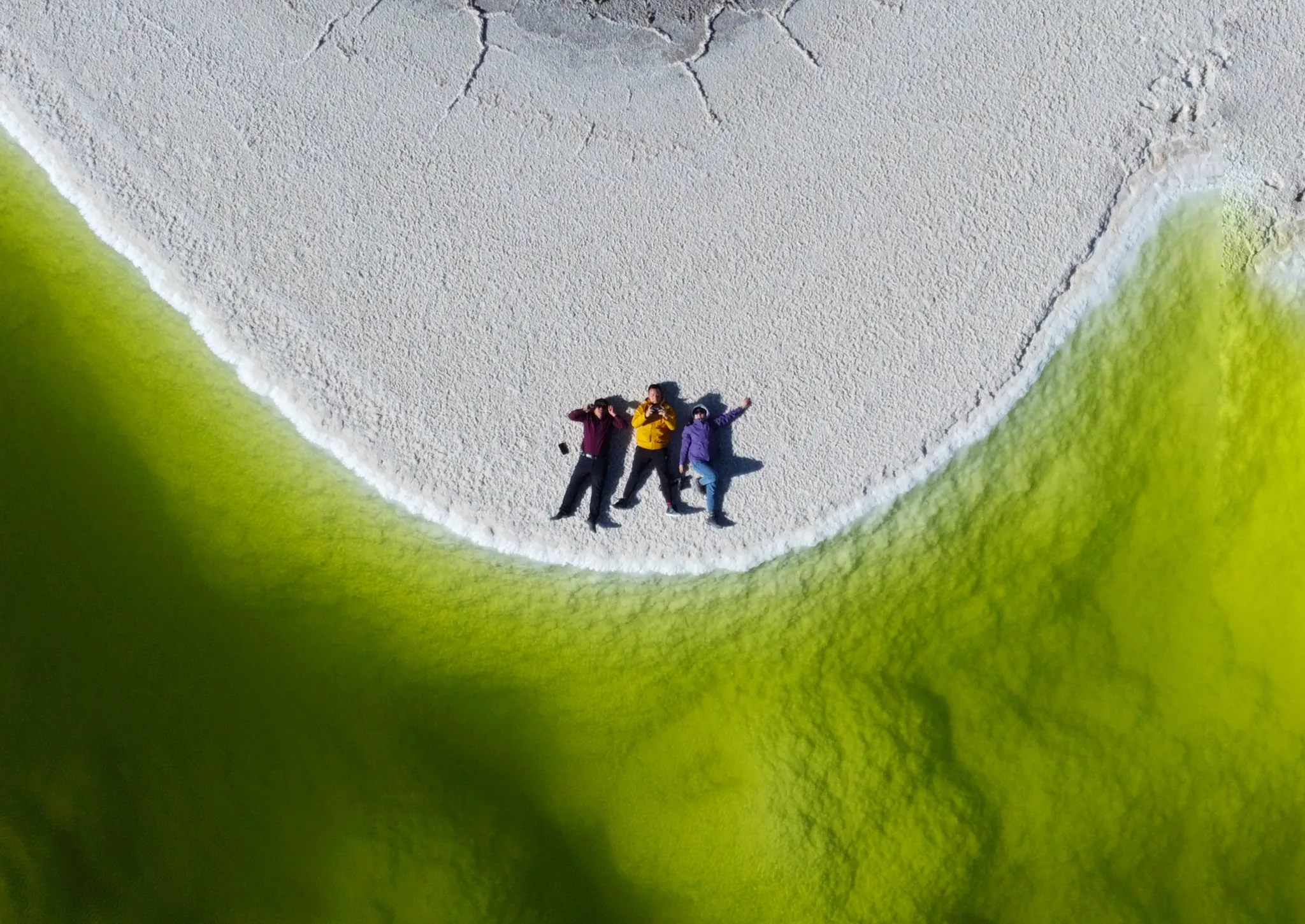 三个人躺在盐湖边，四周是翠绿湖水